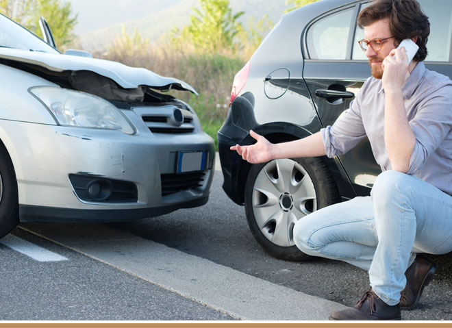 A person talking on a phone next to a wrecked car Description automatically generated